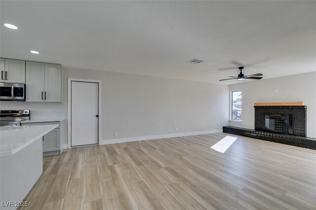 unfurnished living room with light wood-type flooring, ceiling fan, and a fireplace