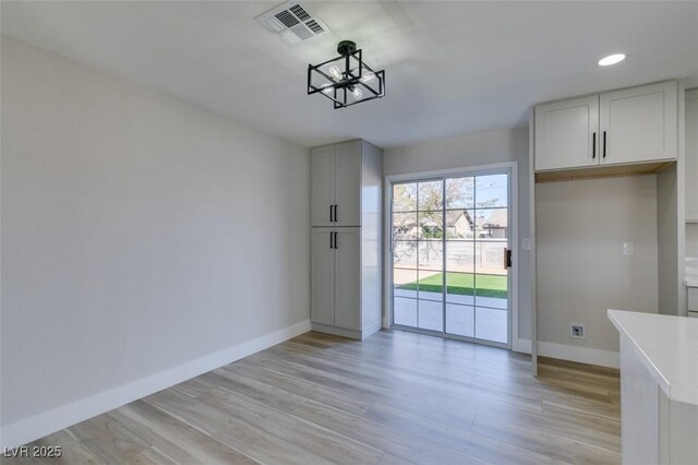 unfurnished dining area with a notable chandelier and light hardwood / wood-style flooring