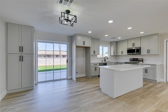 kitchen featuring appliances with stainless steel finishes, gray cabinetry, light wood-type flooring, and a kitchen island