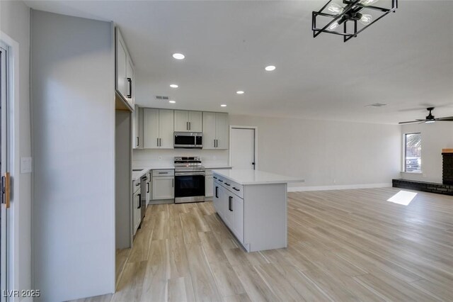 kitchen with appliances with stainless steel finishes, a center island, a fireplace, light hardwood / wood-style floors, and ceiling fan