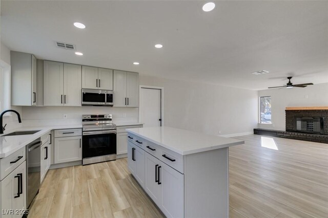 kitchen featuring appliances with stainless steel finishes, a kitchen island, a brick fireplace, sink, and ceiling fan