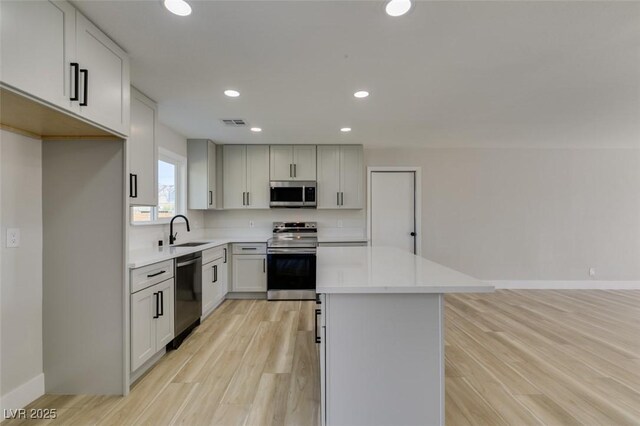 kitchen featuring white cabinets, a center island, stainless steel appliances, light hardwood / wood-style floors, and sink