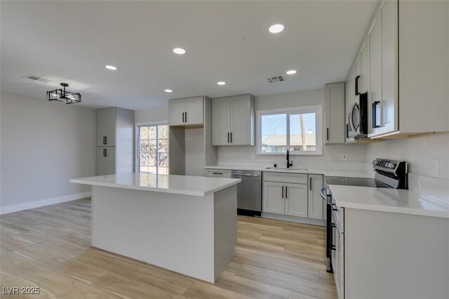 kitchen with an inviting chandelier, stainless steel appliances, a center island, light hardwood / wood-style flooring, and sink