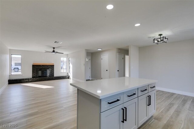 kitchen featuring a fireplace, a kitchen island, light hardwood / wood-style floors, and ceiling fan