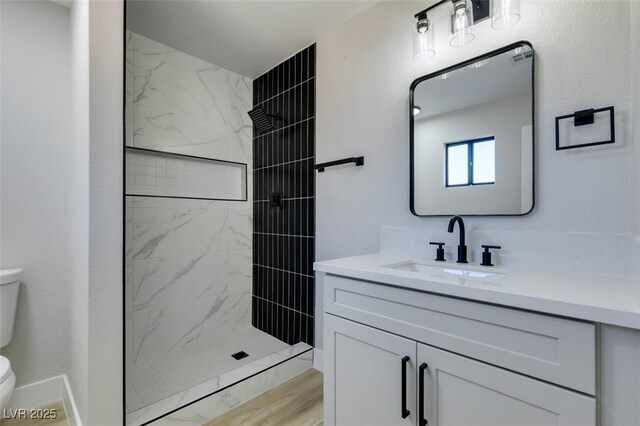 bathroom with toilet, a tile shower, hardwood / wood-style flooring, and vanity