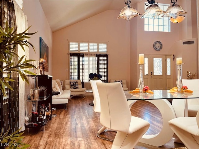 dining area featuring wood-type flooring, a towering ceiling, and an inviting chandelier