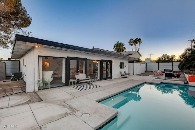 back house at dusk featuring central AC unit, a patio area, and a fenced in pool