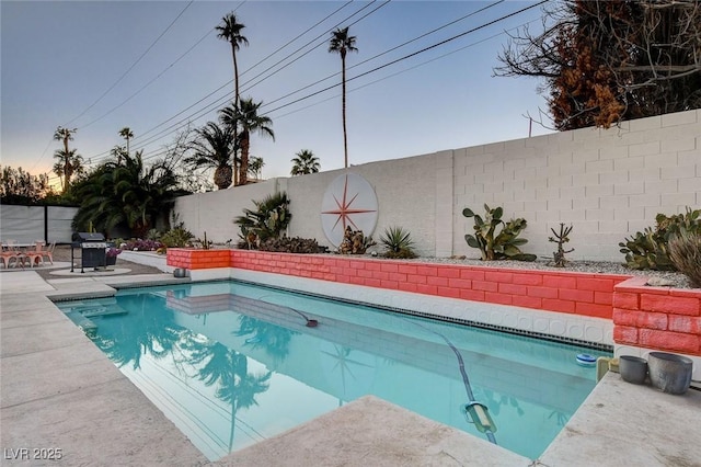 pool at dusk with grilling area and a patio