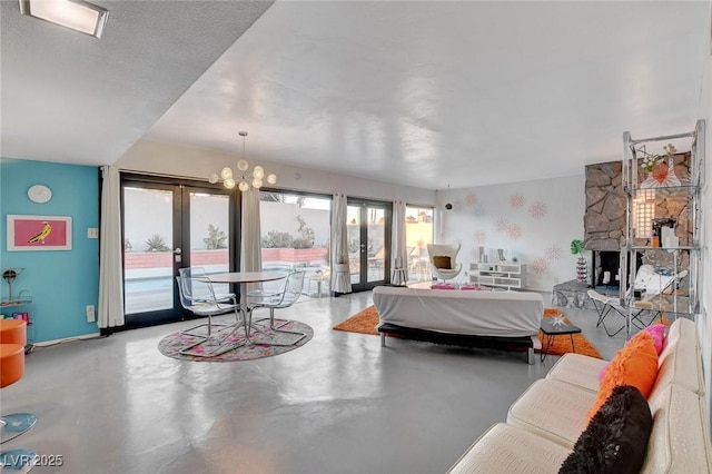 bedroom featuring french doors, access to exterior, an inviting chandelier, and a stone fireplace