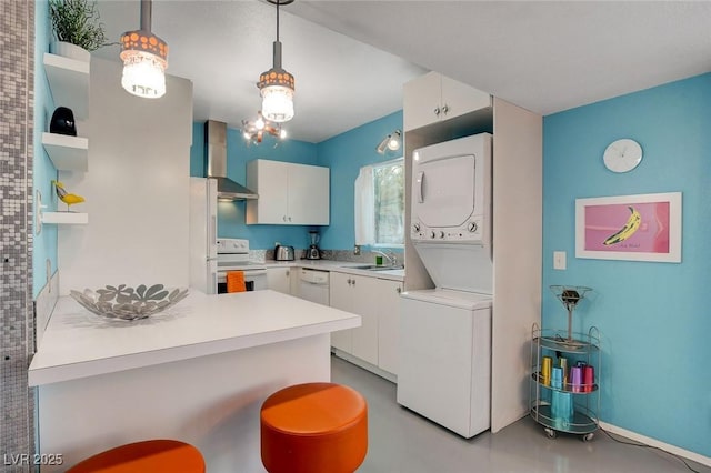 kitchen with white appliances, white cabinets, wall chimney exhaust hood, hanging light fixtures, and stacked washer and clothes dryer