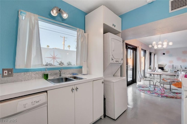 kitchen featuring white cabinets, dishwasher, sink, hanging light fixtures, and stacked washing maching and dryer