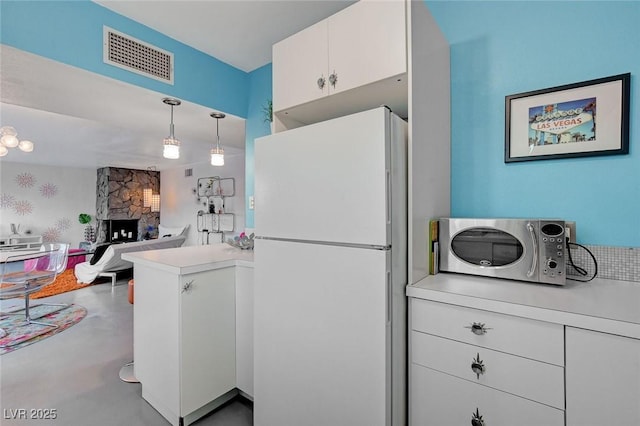 kitchen featuring kitchen peninsula, a stone fireplace, hanging light fixtures, white refrigerator, and white cabinets