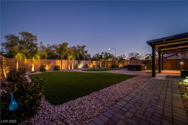 yard at dusk featuring a patio area, a hot tub, and a water view