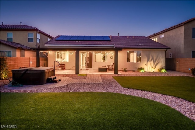 back house at dusk featuring a hot tub, a patio area, and solar panels