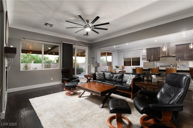 living room with dark wood-type flooring, ornamental molding, and ceiling fan