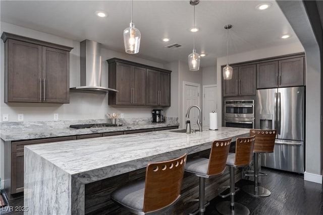 kitchen featuring pendant lighting, a center island with sink, wall chimney exhaust hood, and stainless steel appliances