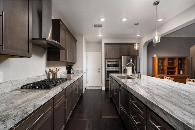 kitchen featuring appliances with stainless steel finishes, wall chimney range hood, sink, hanging light fixtures, and dark brown cabinets