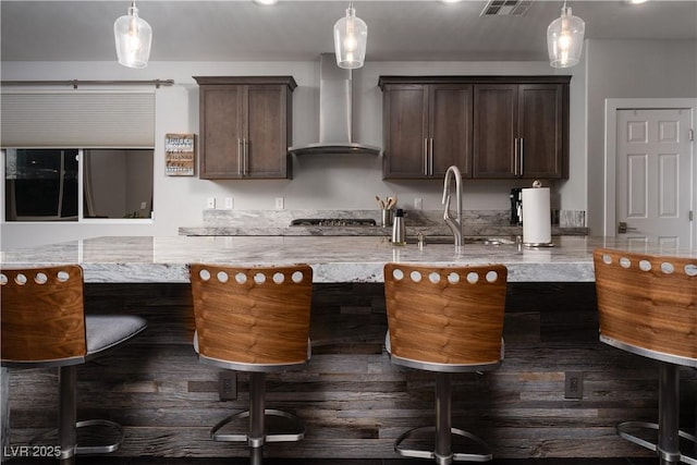 kitchen with wall chimney exhaust hood, dark brown cabinetry, and decorative light fixtures