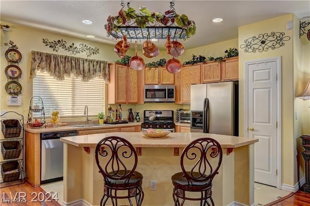 kitchen featuring appliances with stainless steel finishes, a kitchen island, sink, a kitchen breakfast bar, and light wood-type flooring