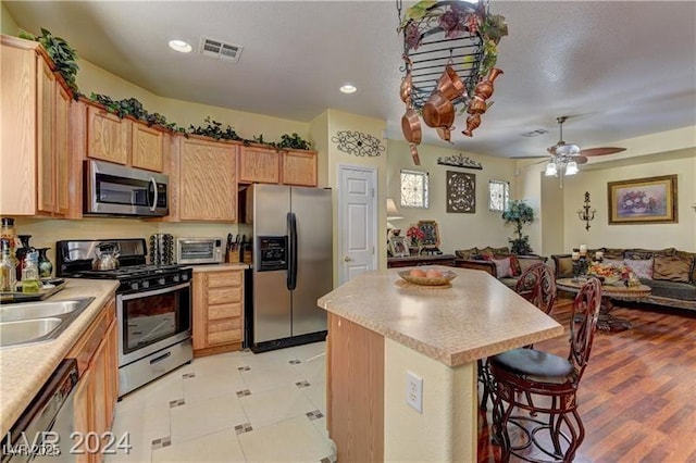 kitchen featuring a breakfast bar area, stainless steel appliances, ceiling fan, light brown cabinets, and a kitchen island