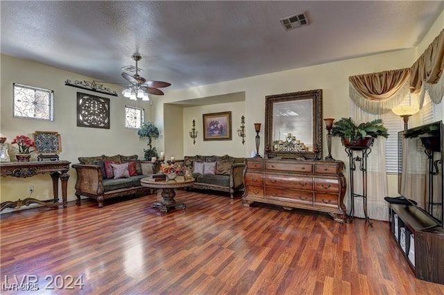 living room featuring ceiling fan, dark wood-type flooring, and a textured ceiling