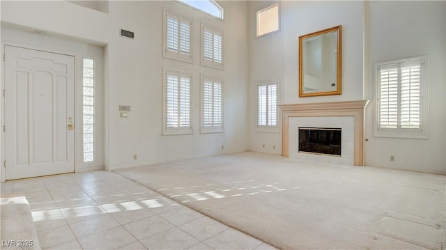 unfurnished living room with light carpet, a towering ceiling, and a tiled fireplace