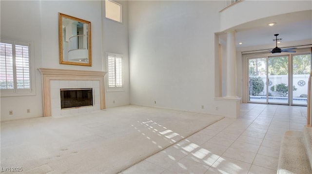 unfurnished living room featuring a towering ceiling, light carpet, a fireplace, ceiling fan, and decorative columns