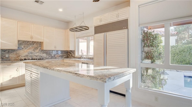 kitchen with backsplash, light stone countertops, a wealth of natural light, and a kitchen island