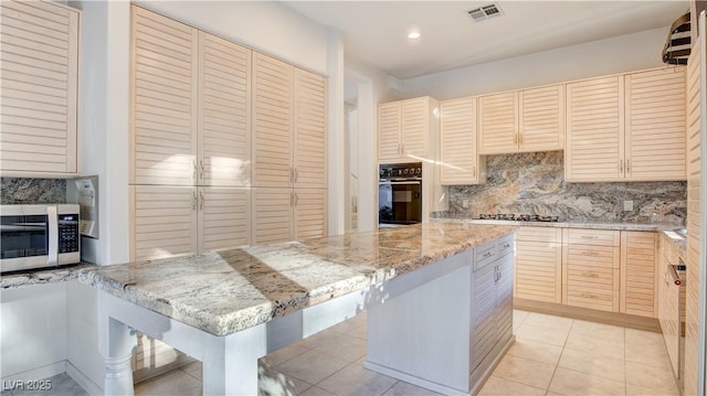 kitchen featuring a kitchen bar, tasteful backsplash, a kitchen island, light stone counters, and black appliances