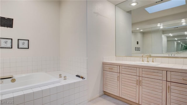 bathroom featuring a skylight, a relaxing tiled tub, and vanity