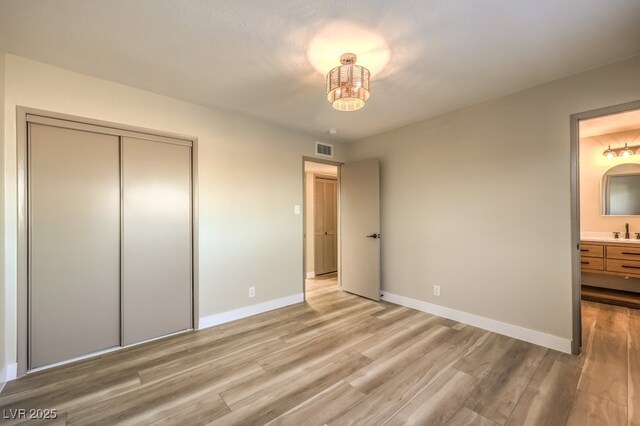 unfurnished bedroom with ensuite bath, a closet, sink, and light hardwood / wood-style floors