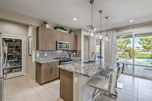 kitchen featuring an island with sink, appliances with stainless steel finishes, tasteful backsplash, decorative light fixtures, and sink