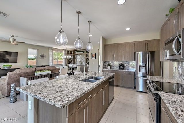 kitchen featuring a center island with sink, ceiling fan, stainless steel appliances, tasteful backsplash, and sink