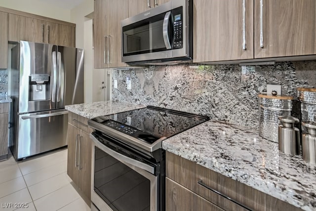 kitchen featuring tasteful backsplash, light tile patterned floors, appliances with stainless steel finishes, and light stone counters