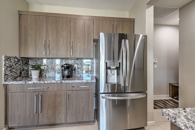 kitchen featuring stainless steel refrigerator with ice dispenser, light stone countertops, decorative backsplash, and light tile patterned floors