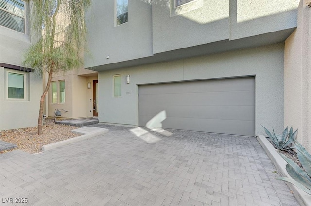 view of front of property featuring decorative driveway, an attached garage, and stucco siding