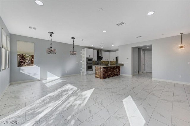 kitchen featuring stainless steel microwave, white cabinets, a kitchen island, and pendant lighting