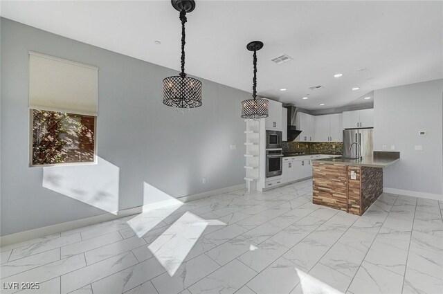 kitchen with white cabinetry, appliances with stainless steel finishes, tasteful backsplash, decorative light fixtures, and wall chimney range hood