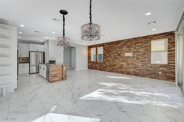 kitchen featuring stainless steel appliances, a kitchen island with sink, pendant lighting, white cabinets, and sink