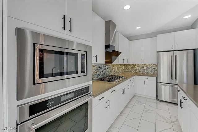 kitchen with decorative backsplash, white cabinetry, appliances with stainless steel finishes, and wall chimney exhaust hood