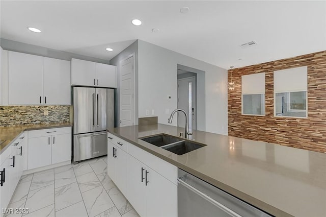 kitchen featuring a sink, marble finish floor, stainless steel appliances, white cabinetry, and backsplash