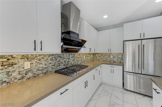 kitchen with tasteful backsplash, white cabinets, appliances with stainless steel finishes, and wall chimney range hood