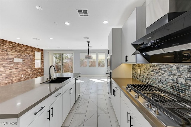 kitchen with white cabinetry, wall chimney range hood, stainless steel appliances, sink, and hanging light fixtures