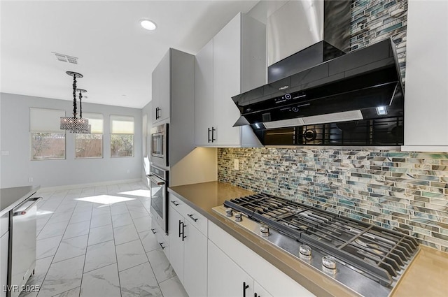 kitchen with appliances with stainless steel finishes, white cabinetry, hanging light fixtures, and wall chimney range hood