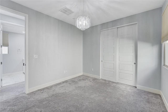 unfurnished bedroom featuring a closet, visible vents, an inviting chandelier, carpet flooring, and baseboards