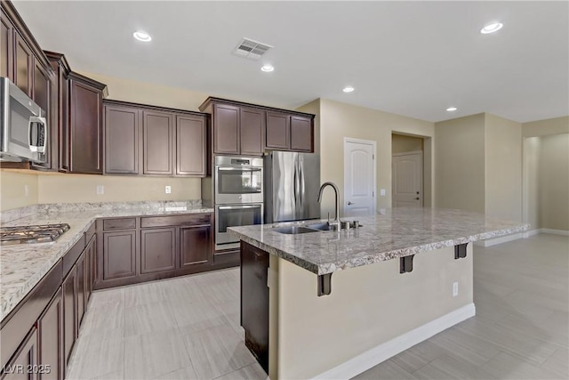 kitchen with a center island with sink, sink, dark brown cabinetry, a kitchen breakfast bar, and stainless steel appliances