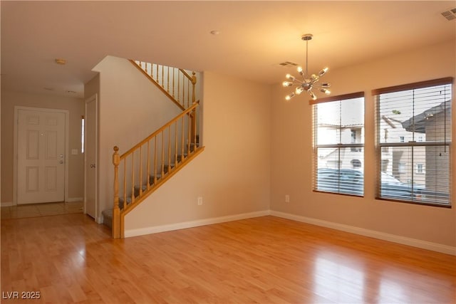 empty room with wood finished floors, visible vents, baseboards, stairway, and an inviting chandelier