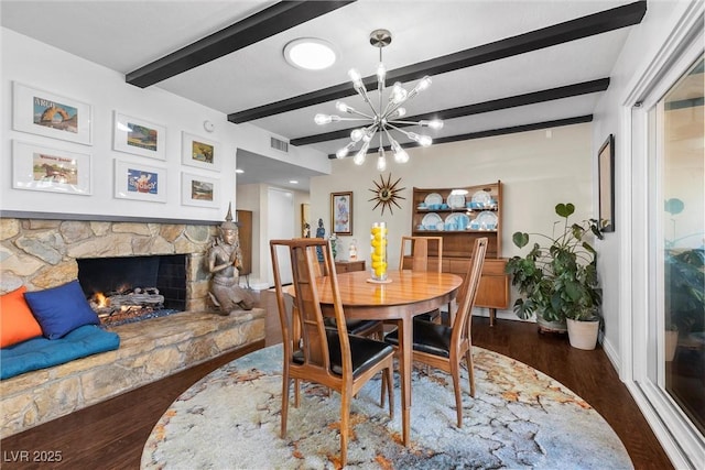 dining space featuring dark wood-type flooring, an inviting chandelier, a fireplace, and beamed ceiling