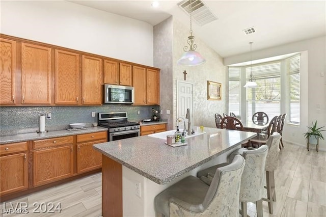 kitchen featuring pendant lighting, appliances with stainless steel finishes, a kitchen breakfast bar, a kitchen island with sink, and high vaulted ceiling