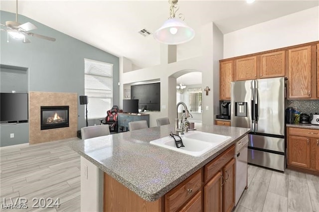 kitchen with ceiling fan with notable chandelier, an island with sink, sink, stainless steel fridge with ice dispenser, and a tile fireplace